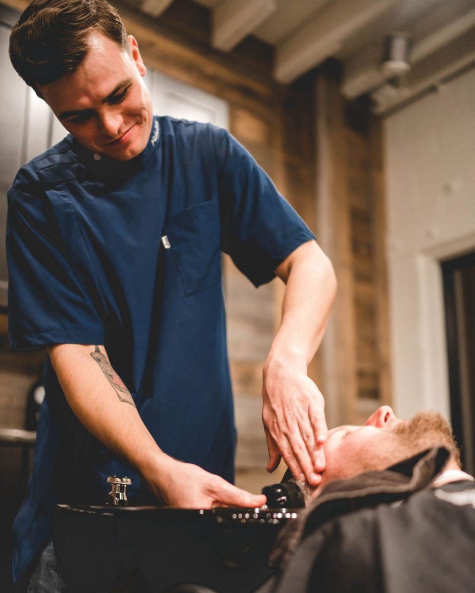 man in fully reclined barber chair having his hair washed in a sink