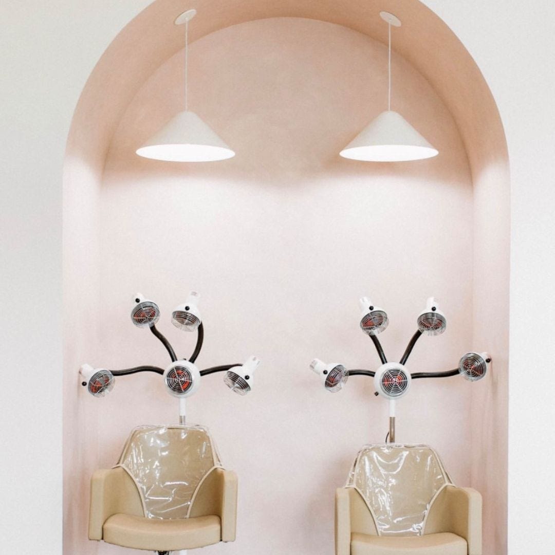 pink wall arch with hair color processors and beige salon chairs