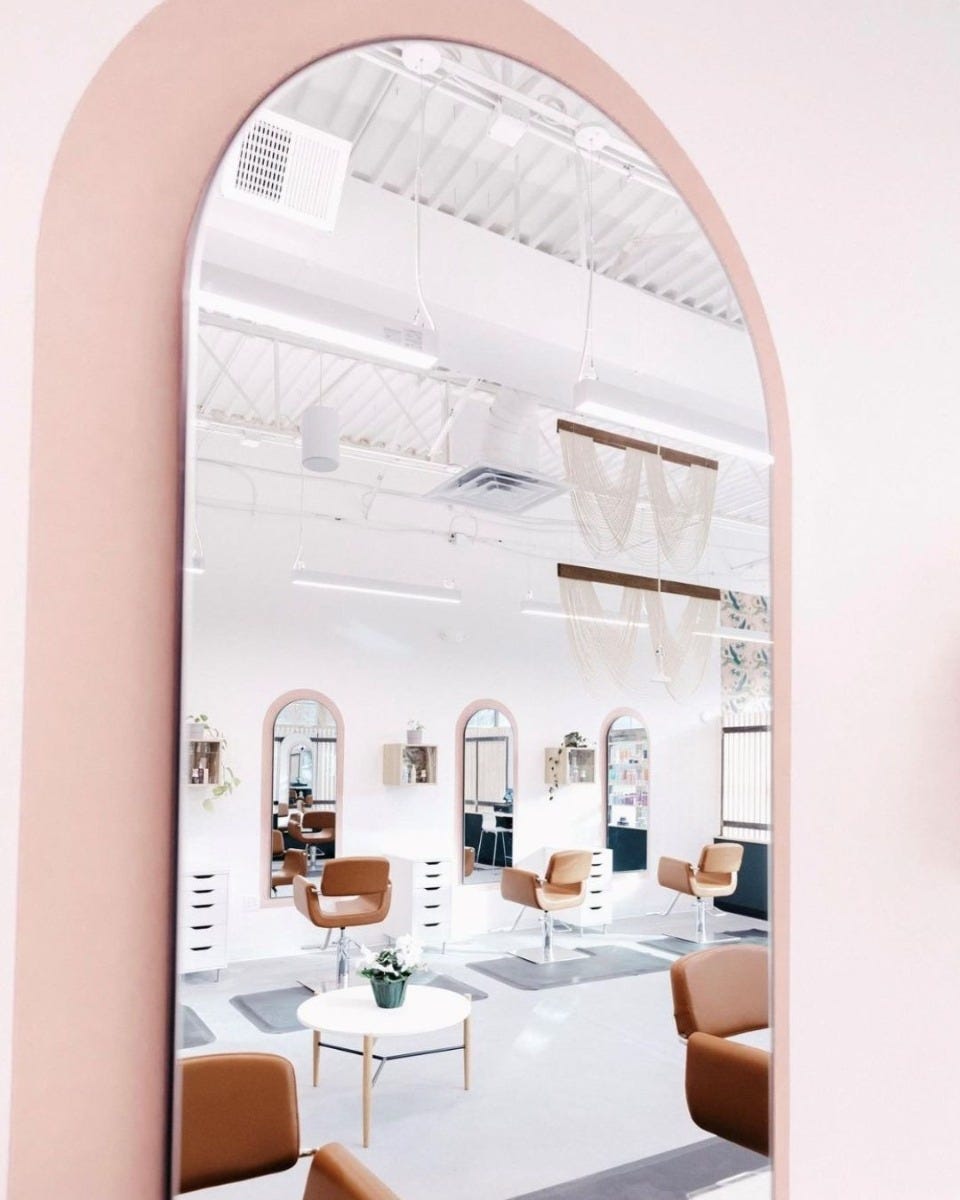 pink wall arch behind salon mirror with brown salon chairs