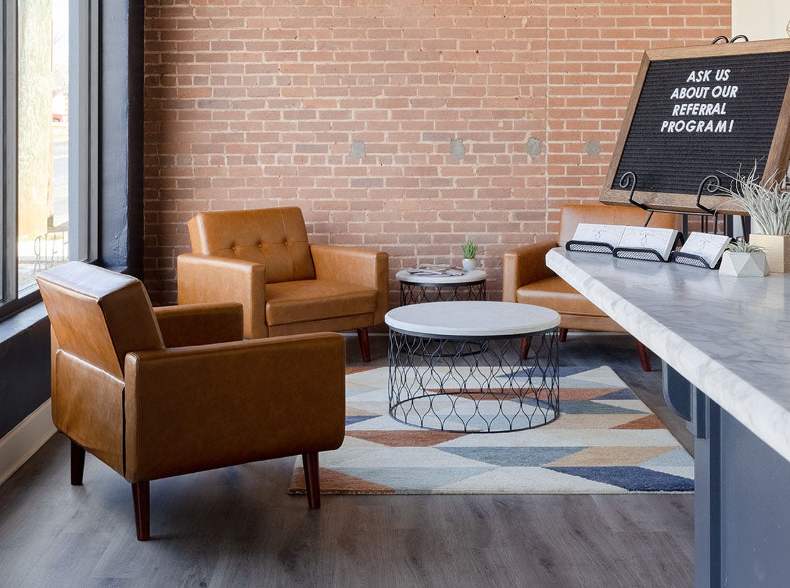 barber shop waiting area with comfortable guest chairs, coffee table and marble top reception desk