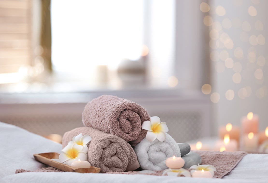 massage room with soft lighting, flowers and rolled towels arranged on massage table