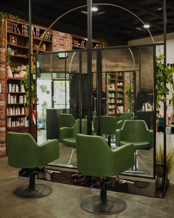 hair salon inteiror with exposed brick walls, plants, large mirrors and spruce green salon styling chairs