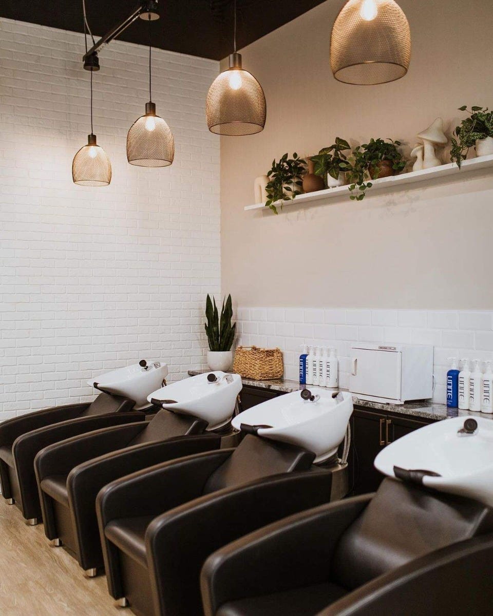 salon shampoo area with four backwash units in dark brown with white bowls, white tiled walls and pendant light fixtures