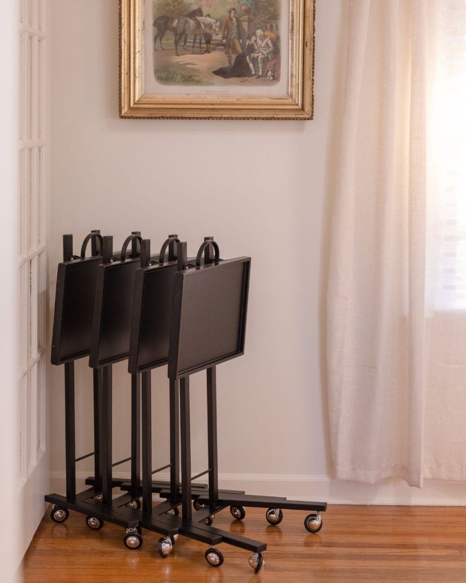 four black metal mobile salon service trays folded down and stored along the wall in a hair salon