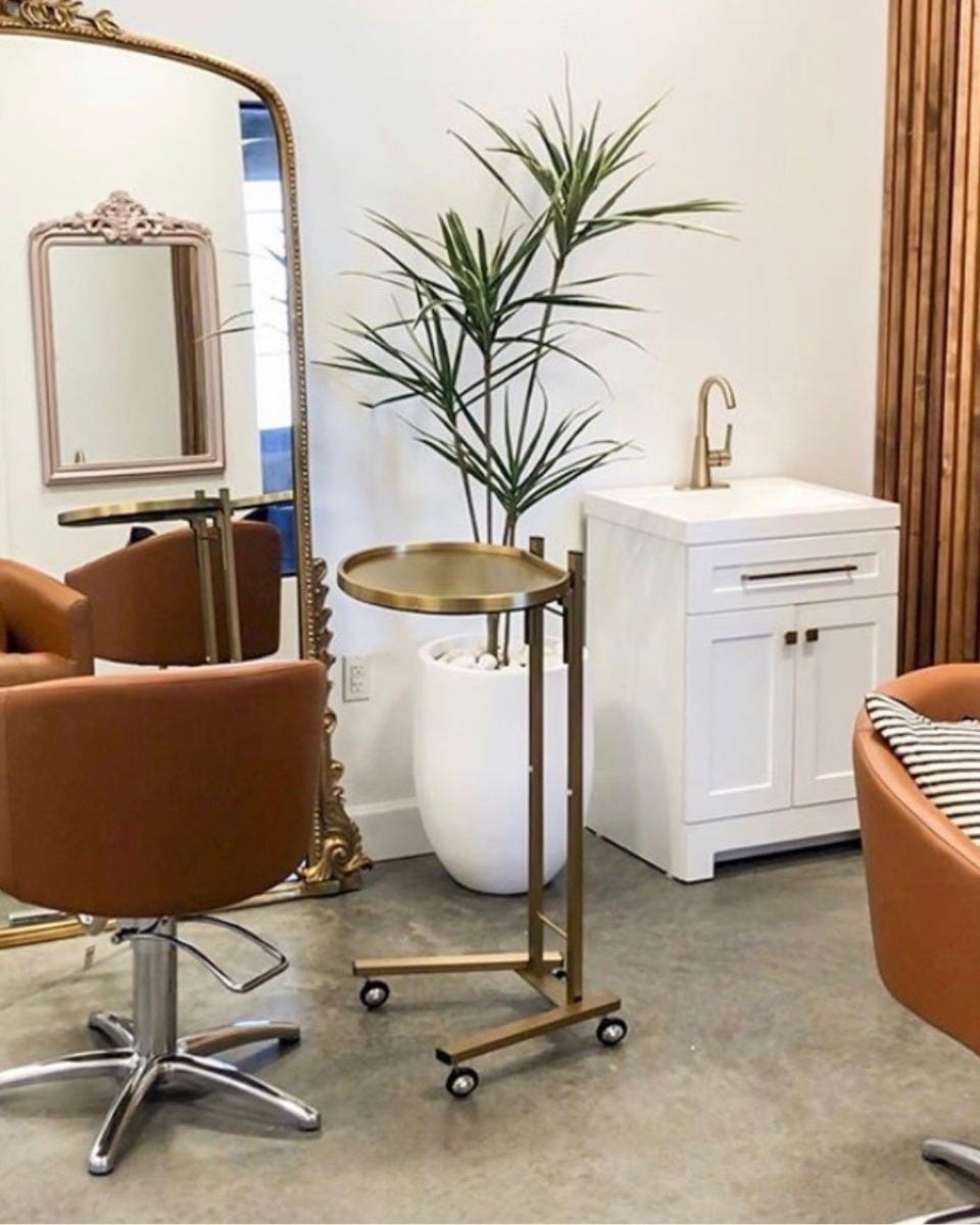 salon station with round gold mobile service tray, tan colored styling chairs and large ornate floor-standing mirrors with gold frames