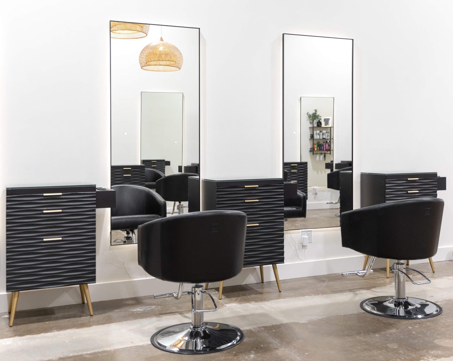 three salon stations with textured pedestal storage furniture and large backlit mirrors