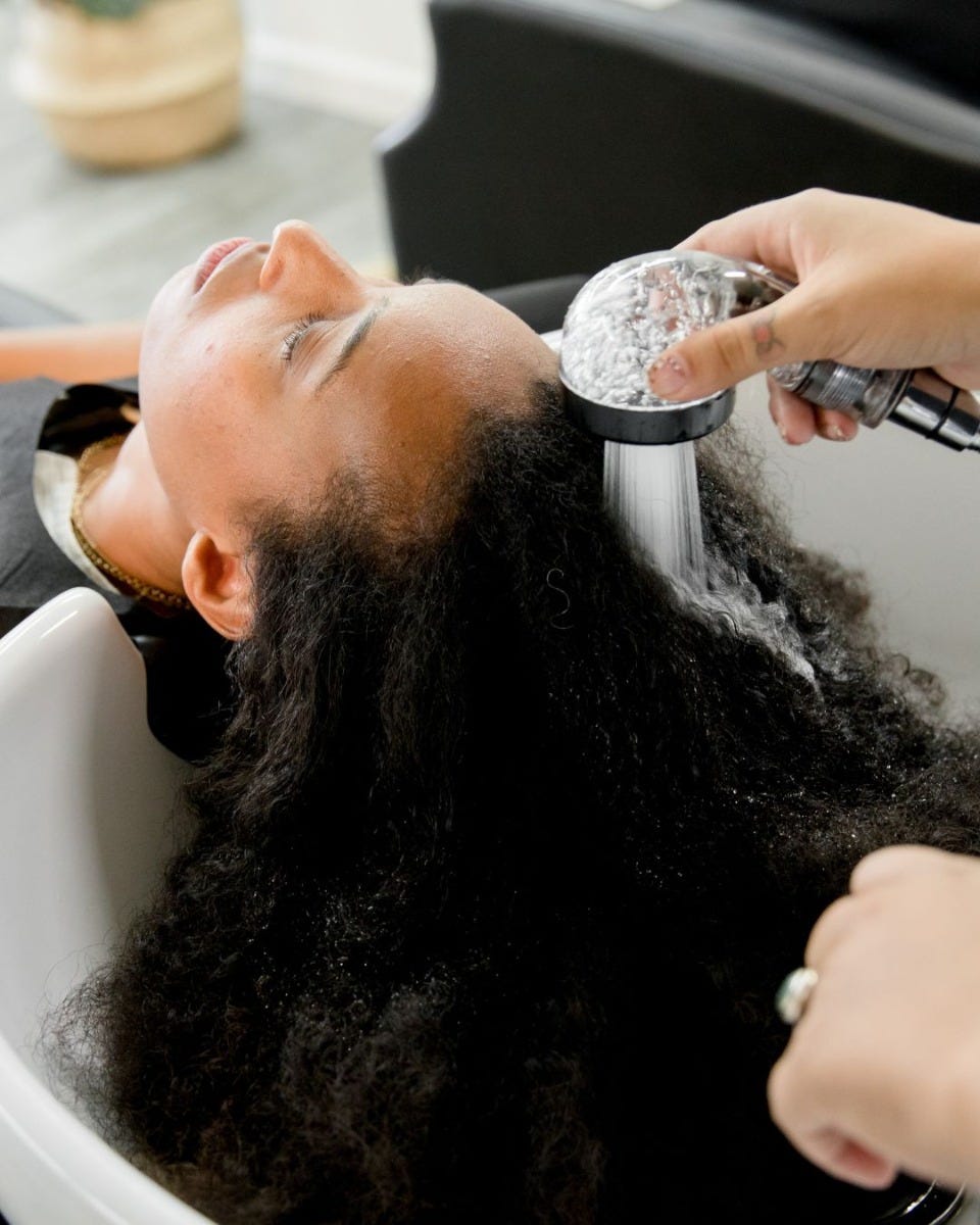 hair stylist using low-flow sprayer to wash client's hair