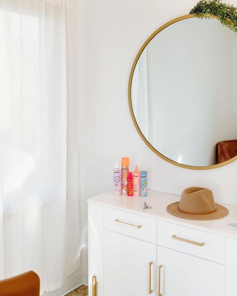 white cabinet styling station with round gold mirror above