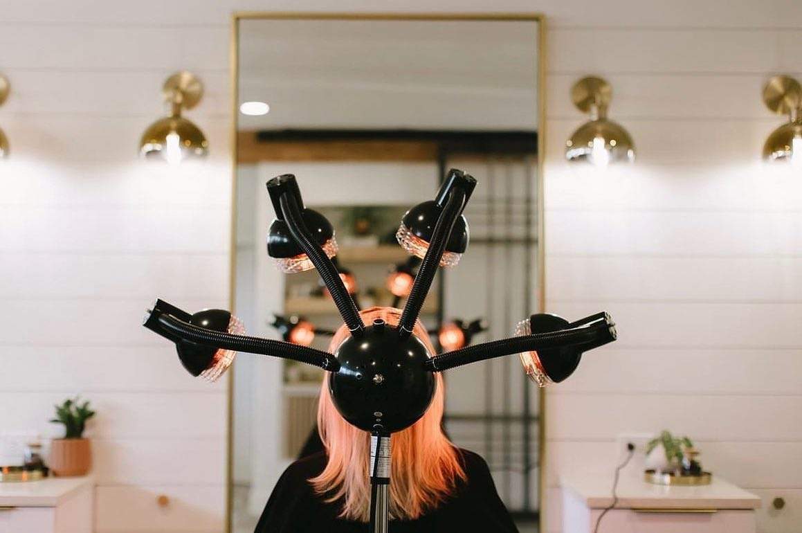 woman with pink hair sitting under hair color processor in a salon