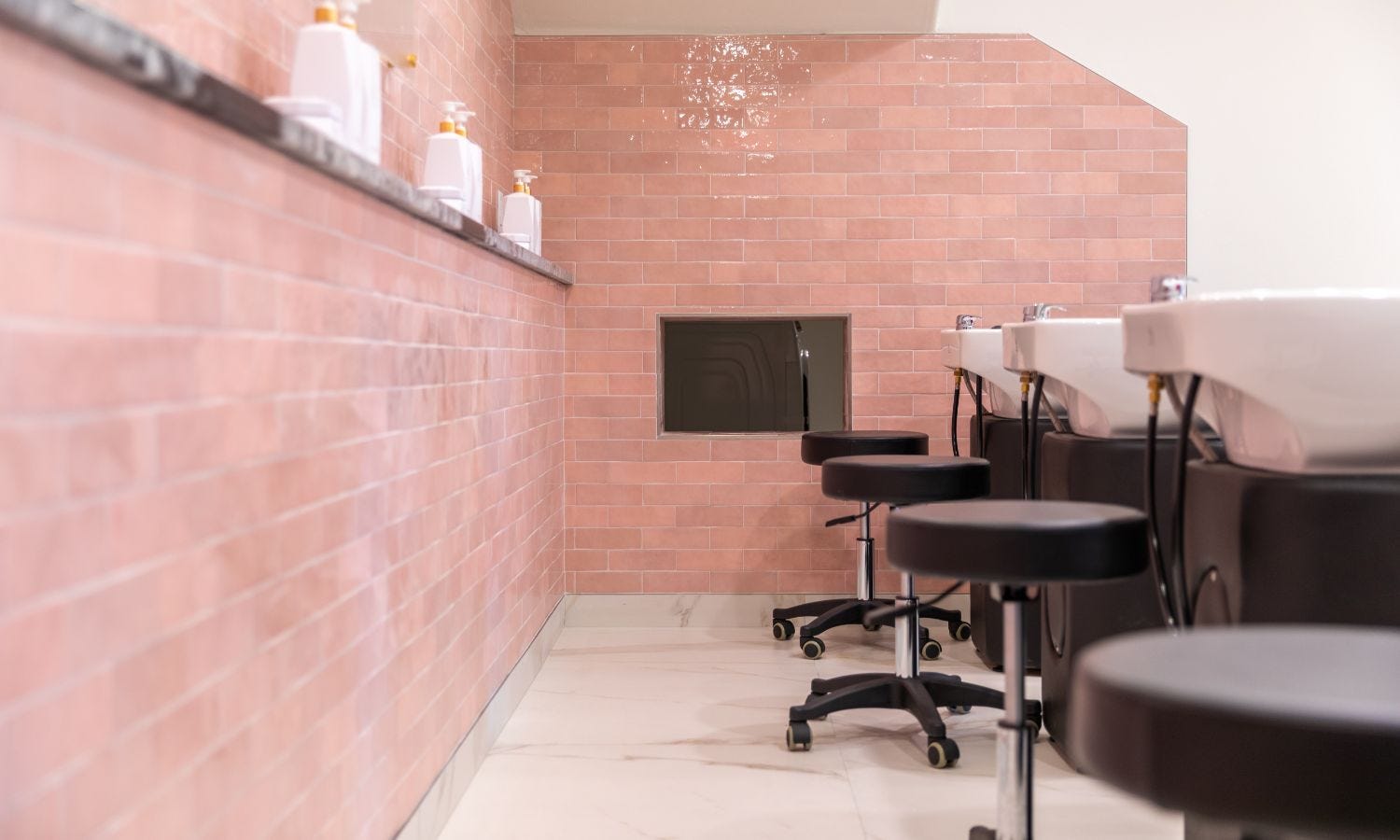 hair salon shampoo area with four wheeled technician stools positioned behind each shampoo station