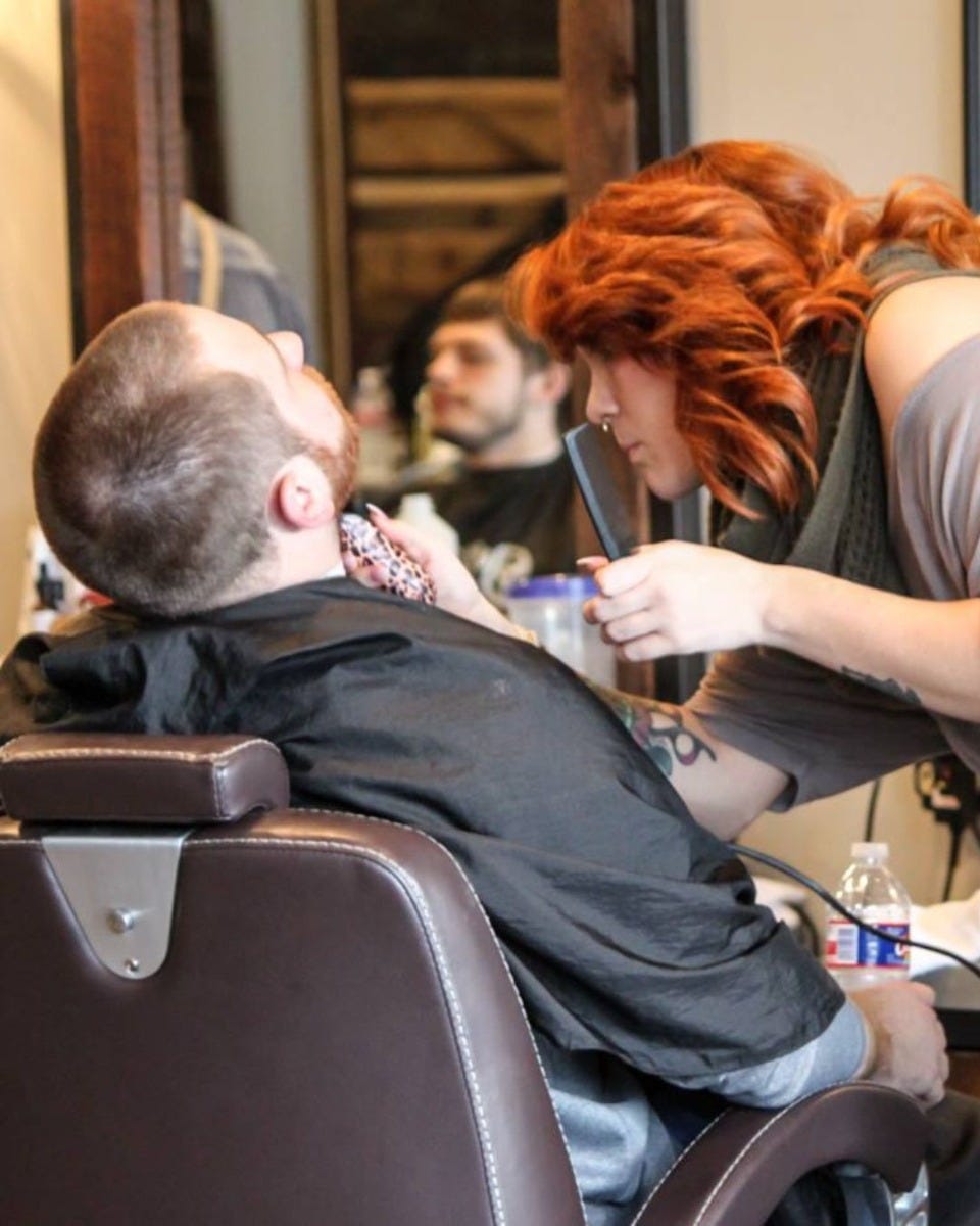 short barber giving a neck trim in a barber chair made for tall clients