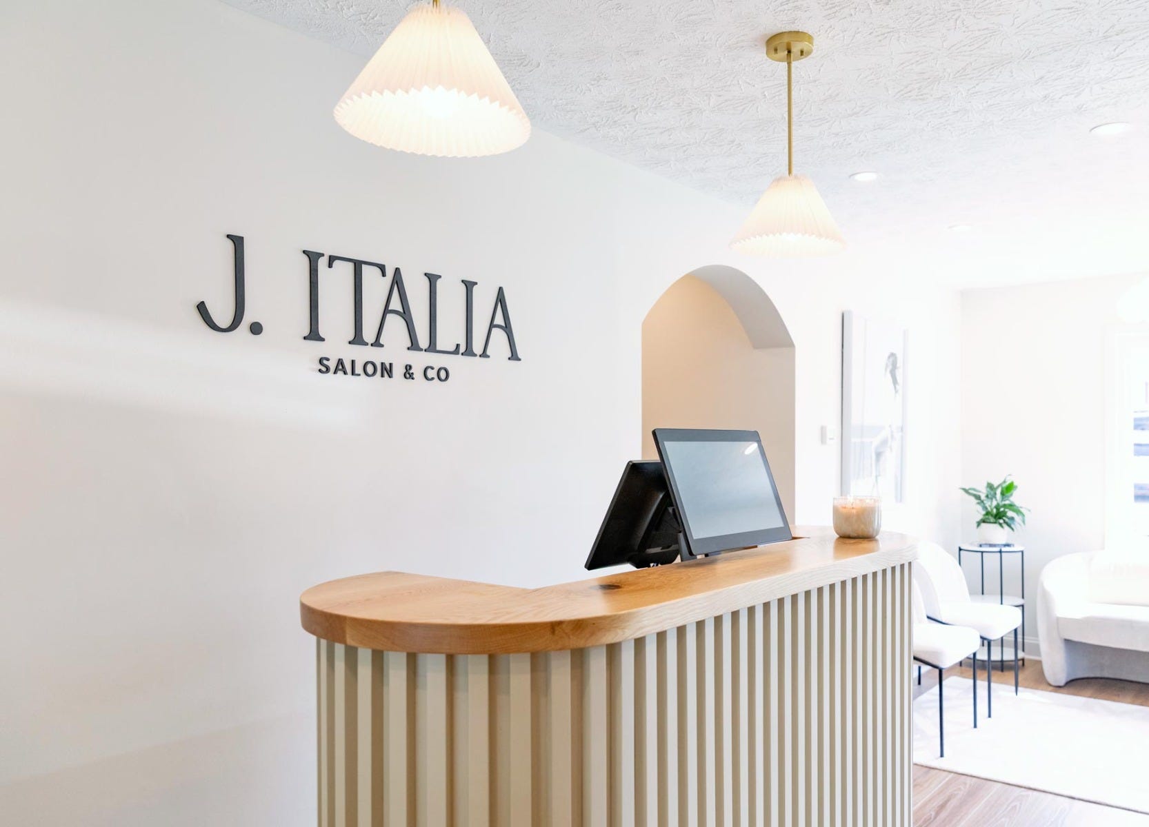 J. Italia Salon reception desk with tablet, pendant lighting, branded signage on wall and nearby waiting area