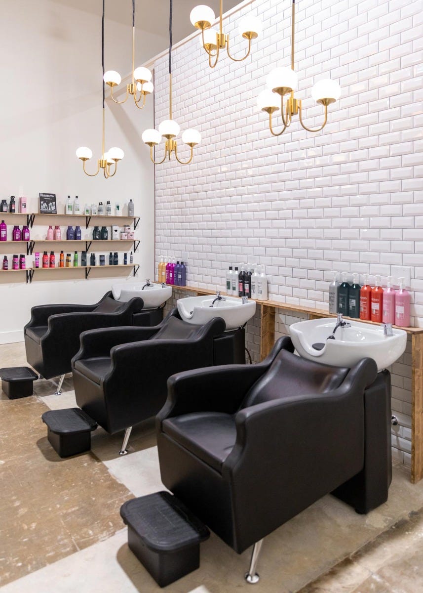 Radiant Salon & Boutique shampoo area with three shampoo backwashes, retail shelving and gold chandelier lighting